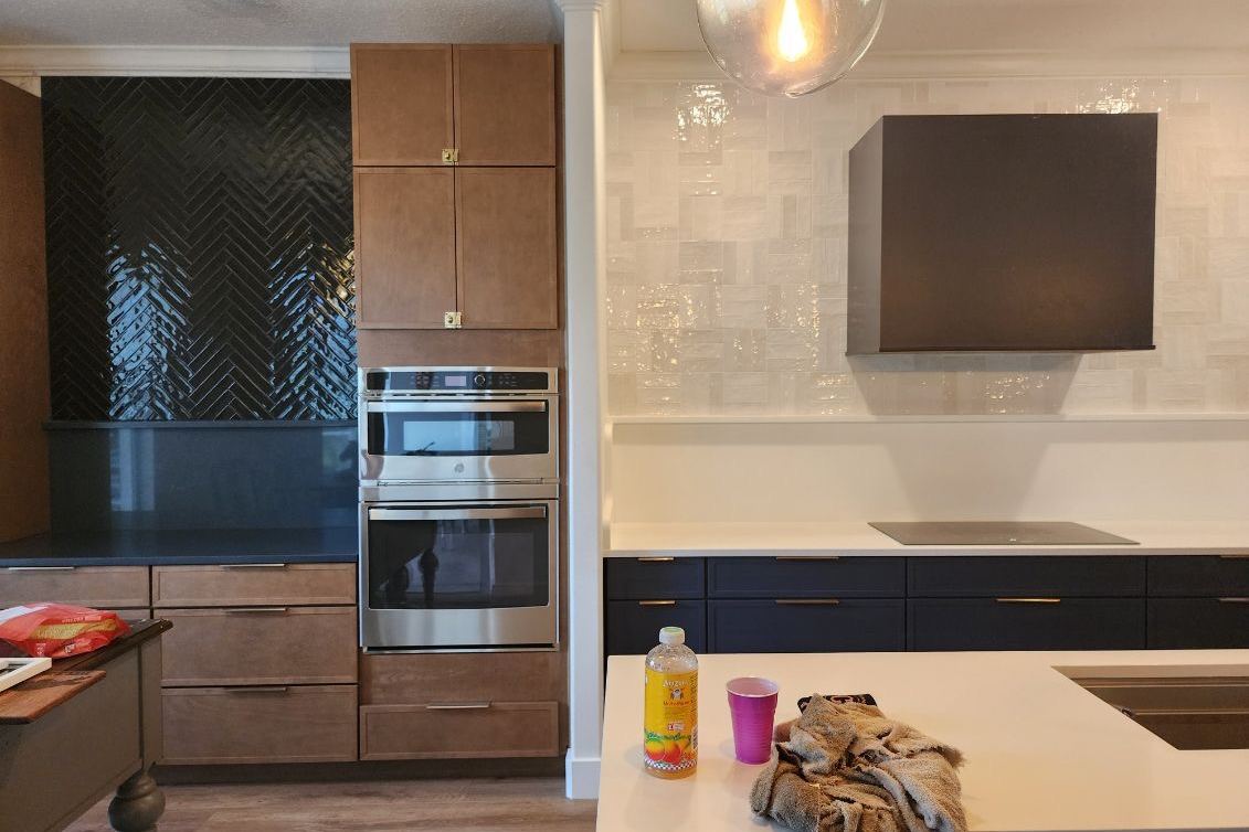 The kitchen finished, with wood cabinetry, a dark tile backsplash and double ovens