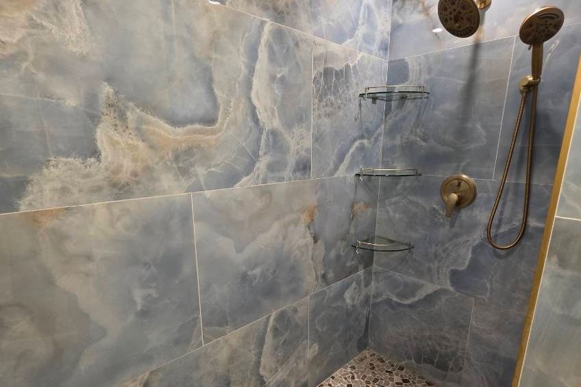Walk-in shower tiled in dark marble with brass fixtures