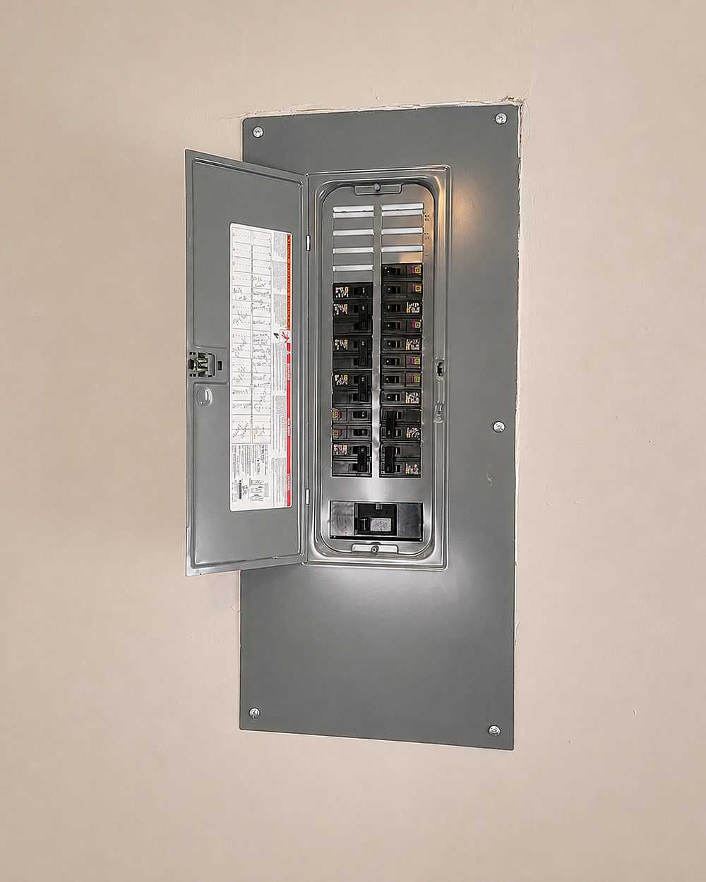 Replacement breaker panel set into a wall, cover open, circuits labelled