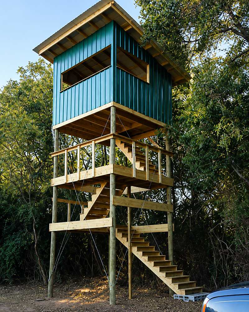 Elevated timber stand on posts, with a stair run, guardrails and a metal-clad cabin on top